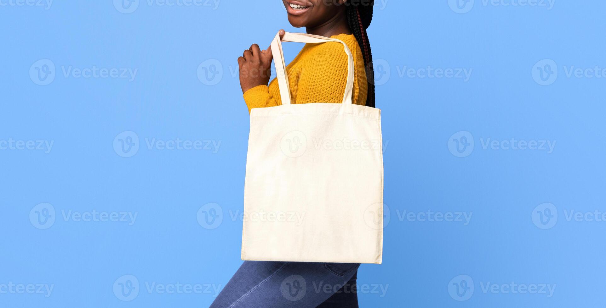 Blank eco tote canvas bag for mockup design in hands of positive black woman standing over purple background in studio and smiling at camera, ecology or environment protection concept, copy space photo