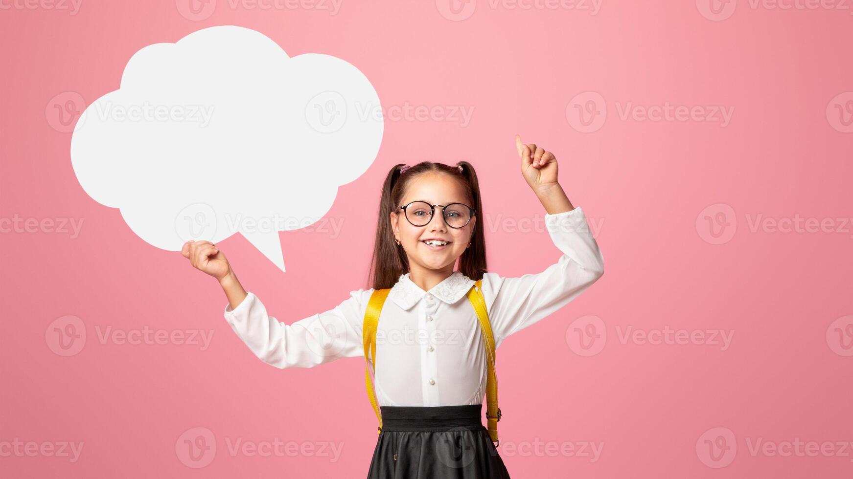 Modern school girl life. Smiling girl in school uniform and glasses points up to empty space and holds abstract word cloud, isolated on pink background photo