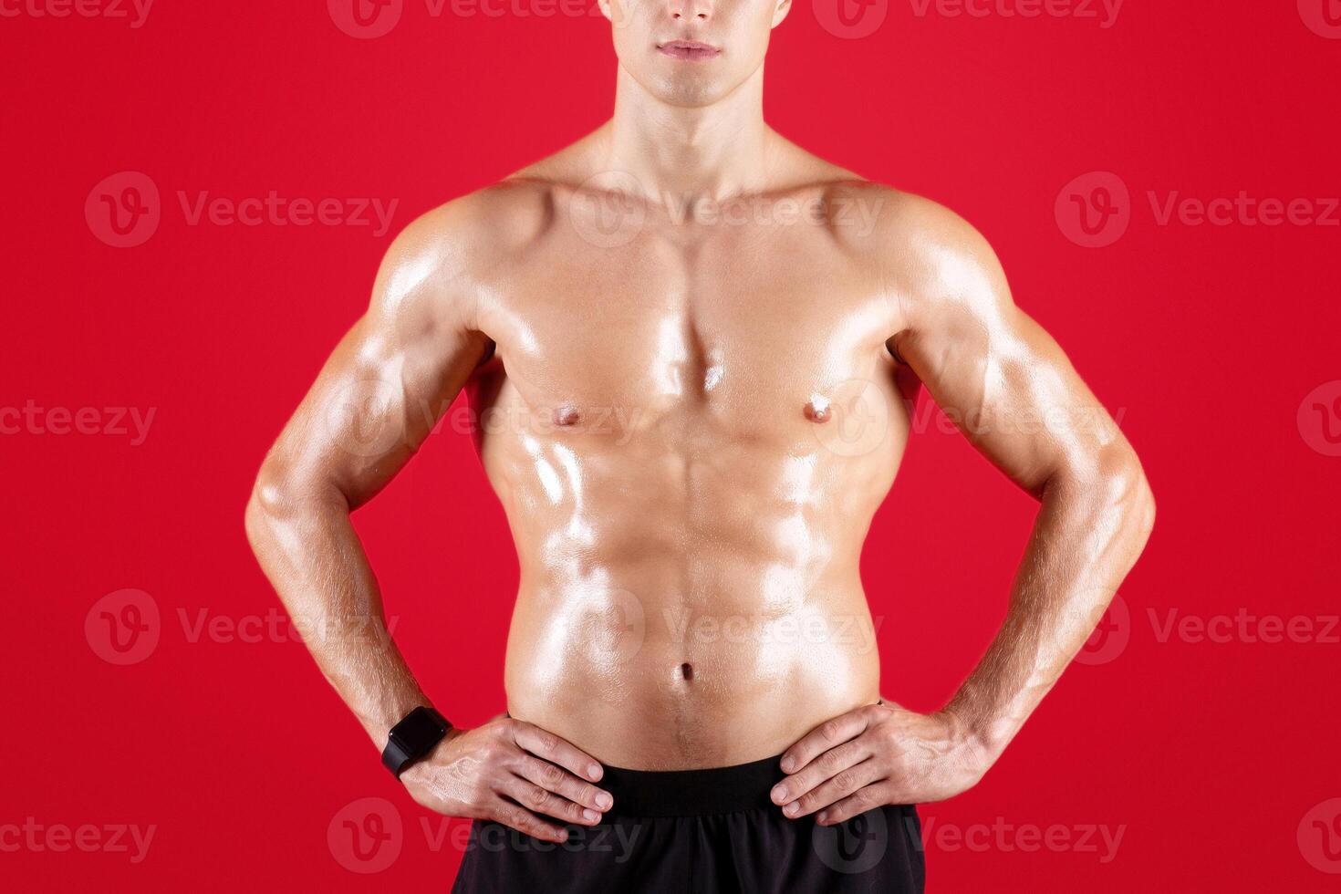 Handsome muscular young man with bare torso posing on red studio background. Serious millennial bodybuilder with shirtless chest and prominent muscles looking at camera. Sports and fitness concept photo
