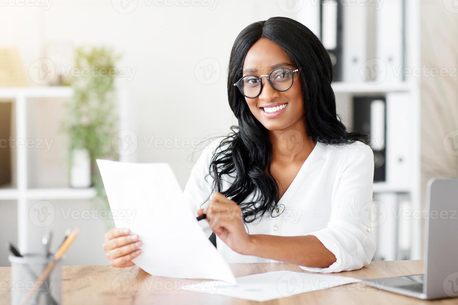 Beautuful black business lady working with documents at desk in office. African American female entrepreneur looking frough important contract or agreement at her workplace photo