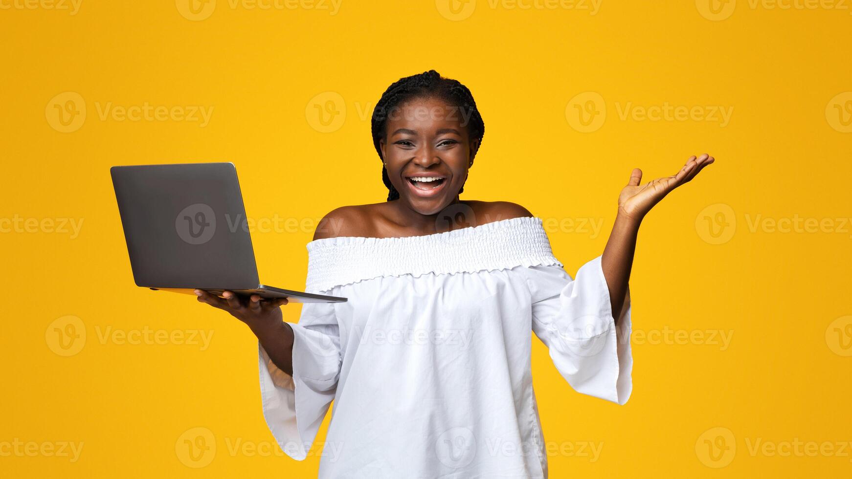 Happy Black Woman Holding Laptop And Exclaiming With Excitement, Celebrating Online Win, Lucky African American Lady Holding PC And Smiling At Camera, Posing Over Yellow Background, Copy Space photo