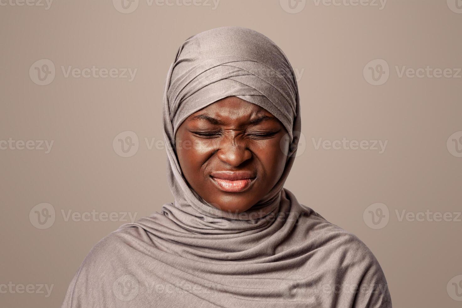 Negative Emotion. Portrait Of Irritated Black Muslim Lady In Hijab Grimacing With Displeased Face Expression Over Light Studio Background, Closeup Of Annoyed African Woman In Headscarf, Copy Space photo