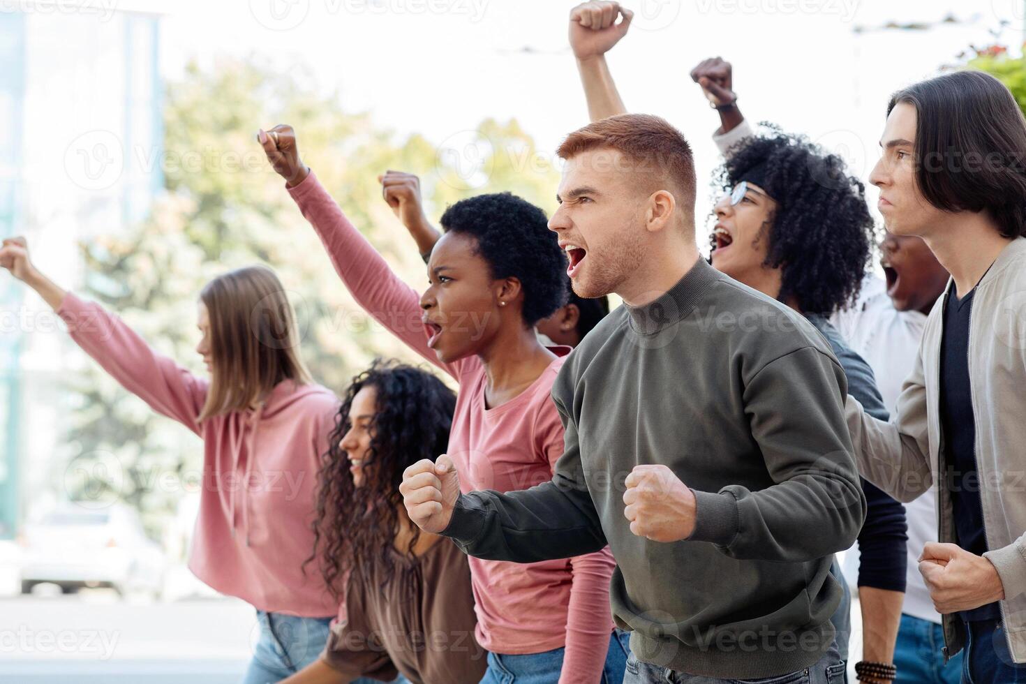 Side view of multiracial group of students chanting slogans and showing fists during demonstration, fighting against reforms in education, copy space. Students rally, demonstration, strike concept photo