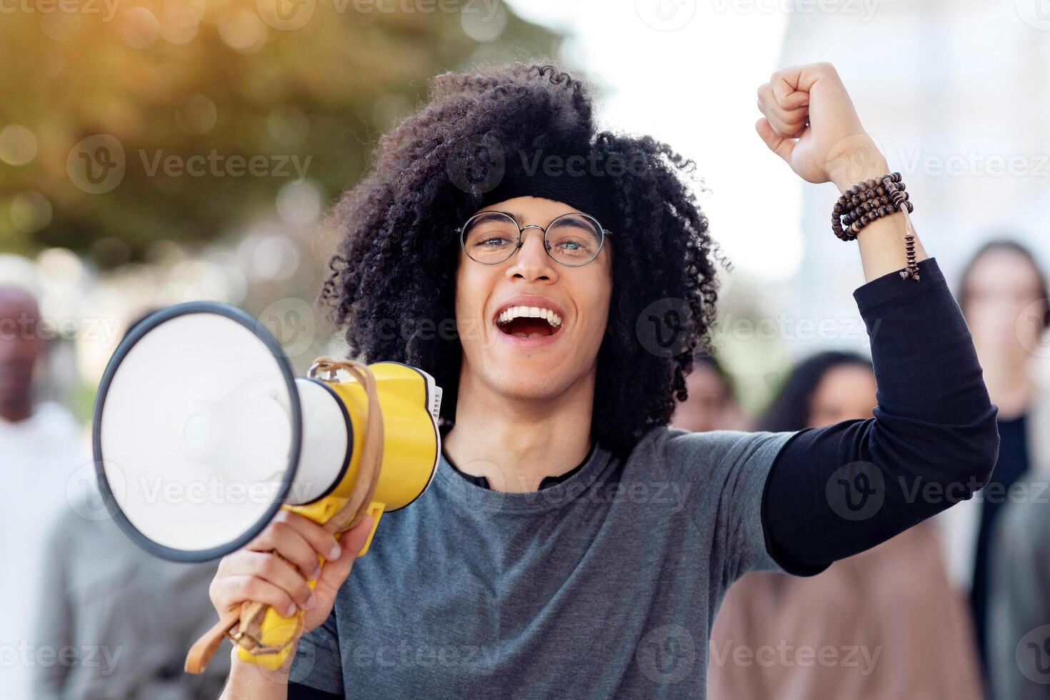 Charismatic black guy activist with megaphone on the street, chanting slogans and raising fist up, young african american man leading international group of activists, striking against lockdown rules photo