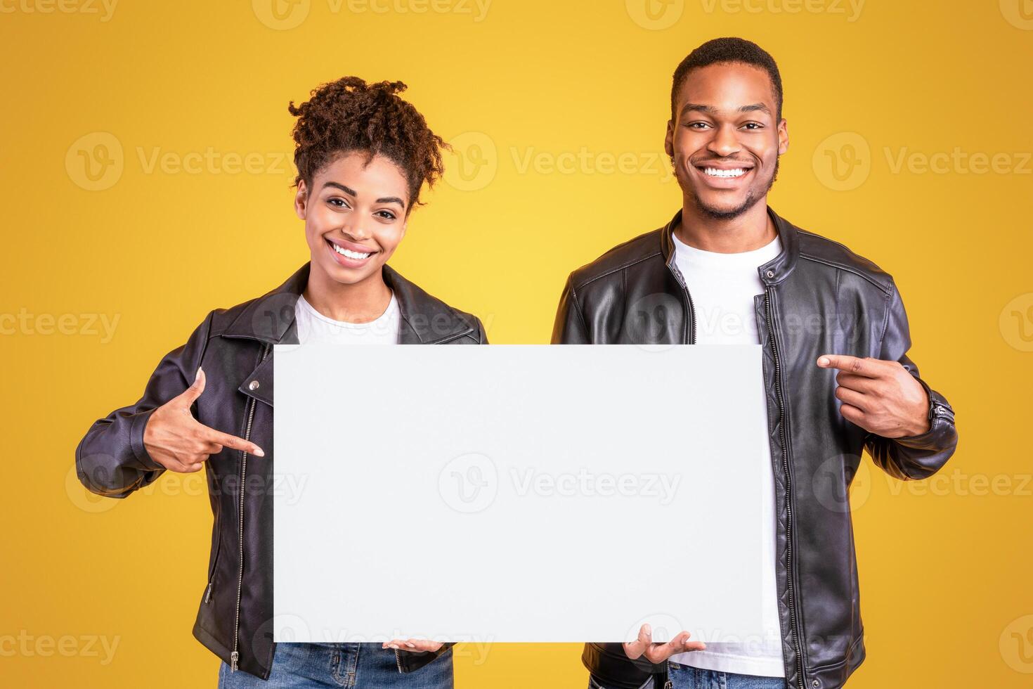 Smiling African American Couple Showing Empty White Board Pointing Fingers At Copy Space For Text Advertising Something Standing On Yellow Background, Studio Shot. Advertisement Banner photo