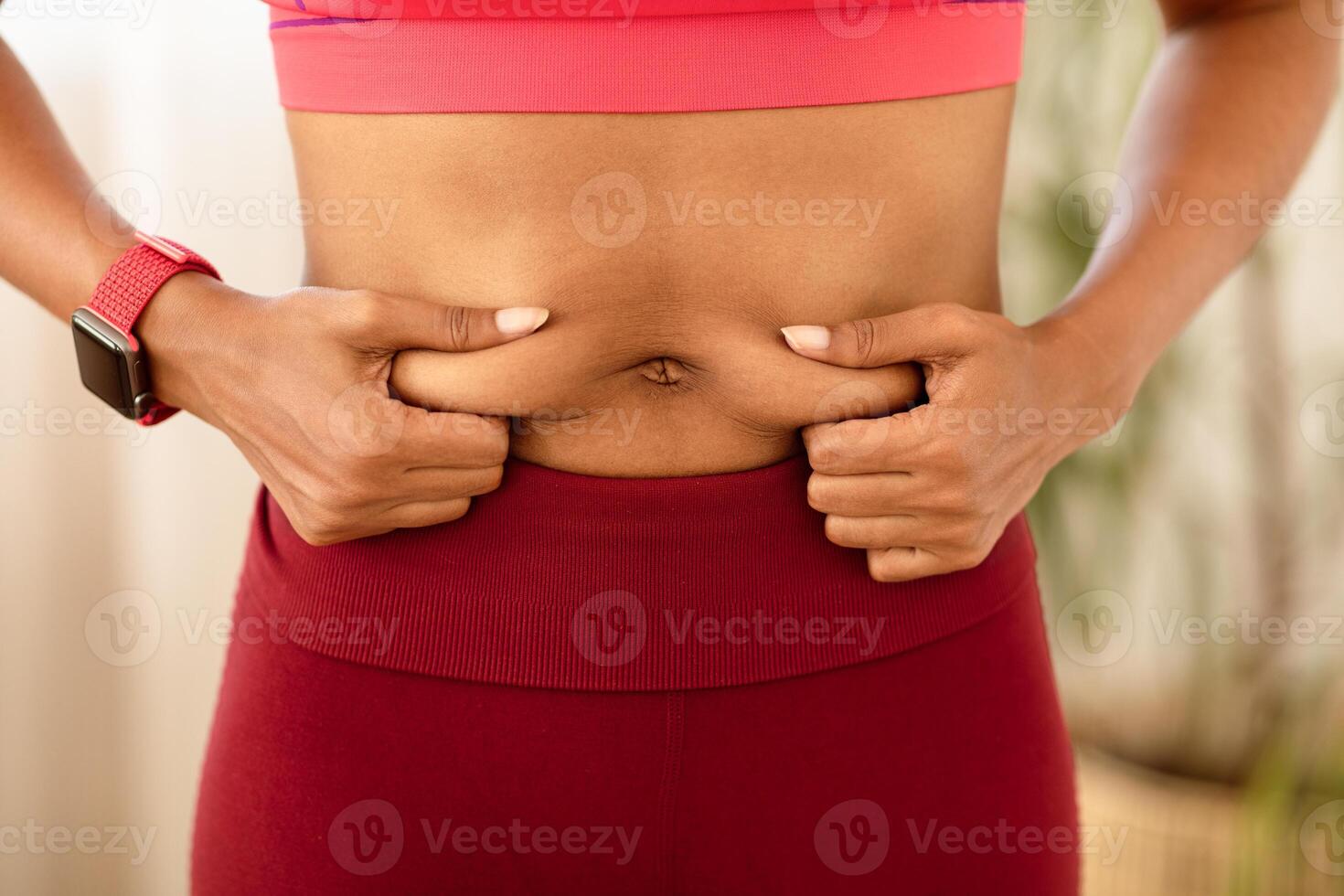 Belly Fat. Unrecognizable Black Woman Touching Stomach Losing Weight, Wearing Fitwear Standing Indoors. Cropped photo