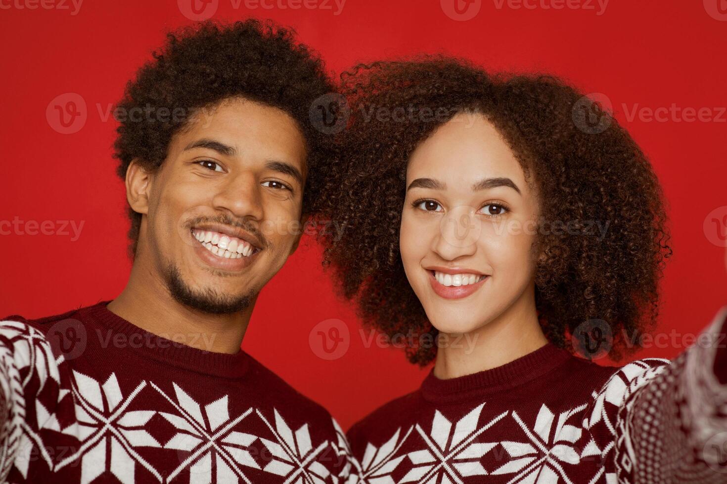 Selfie photo of couple on smartphone and celebrating new year and christmas during self-isolation in quarantine covid-19. Happy male and female in sweaters looking at camera isolated on red background
