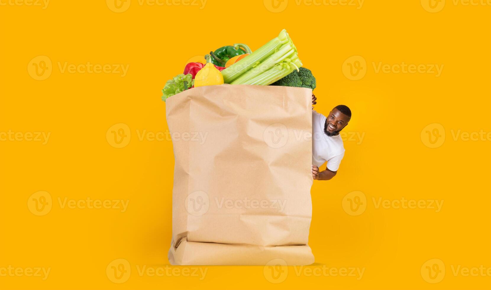 A customer joyfully engages with a large paper bag full of fresh vegetables and fruits. The vibrant background highlights the shift towards online shopping and home delivery services in daily life. photo