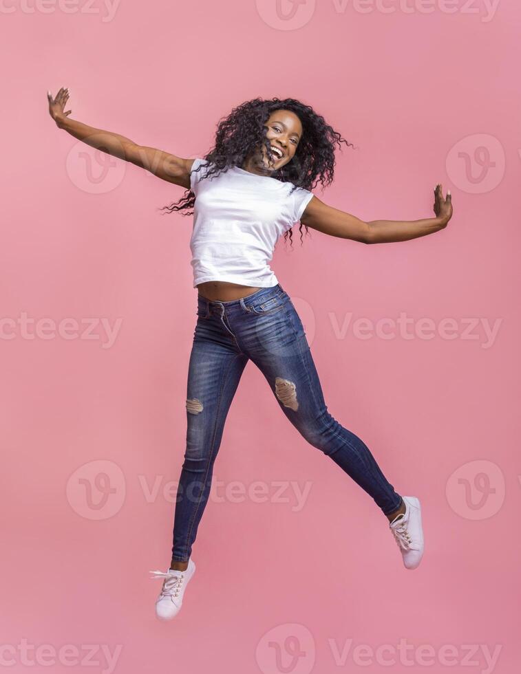 Carefree attractive black girl jumping in the air, pretending she is flying, pink background photo
