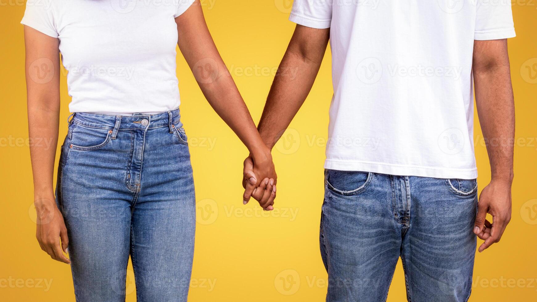 Happy African American Couple In Santa Hats Holding Hands Celebrating Christmas Posing Standing Over Yellow Background, Smiling Each Other. Xmas, Winter Holidays And New Year Celebration. Studio Shot photo