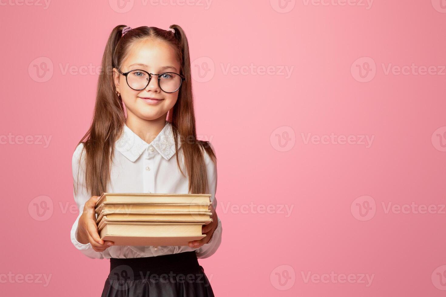 Nerd and smart kid. Cute little schoolgirl in glasses and uniform holds books, isolated on pink background photo