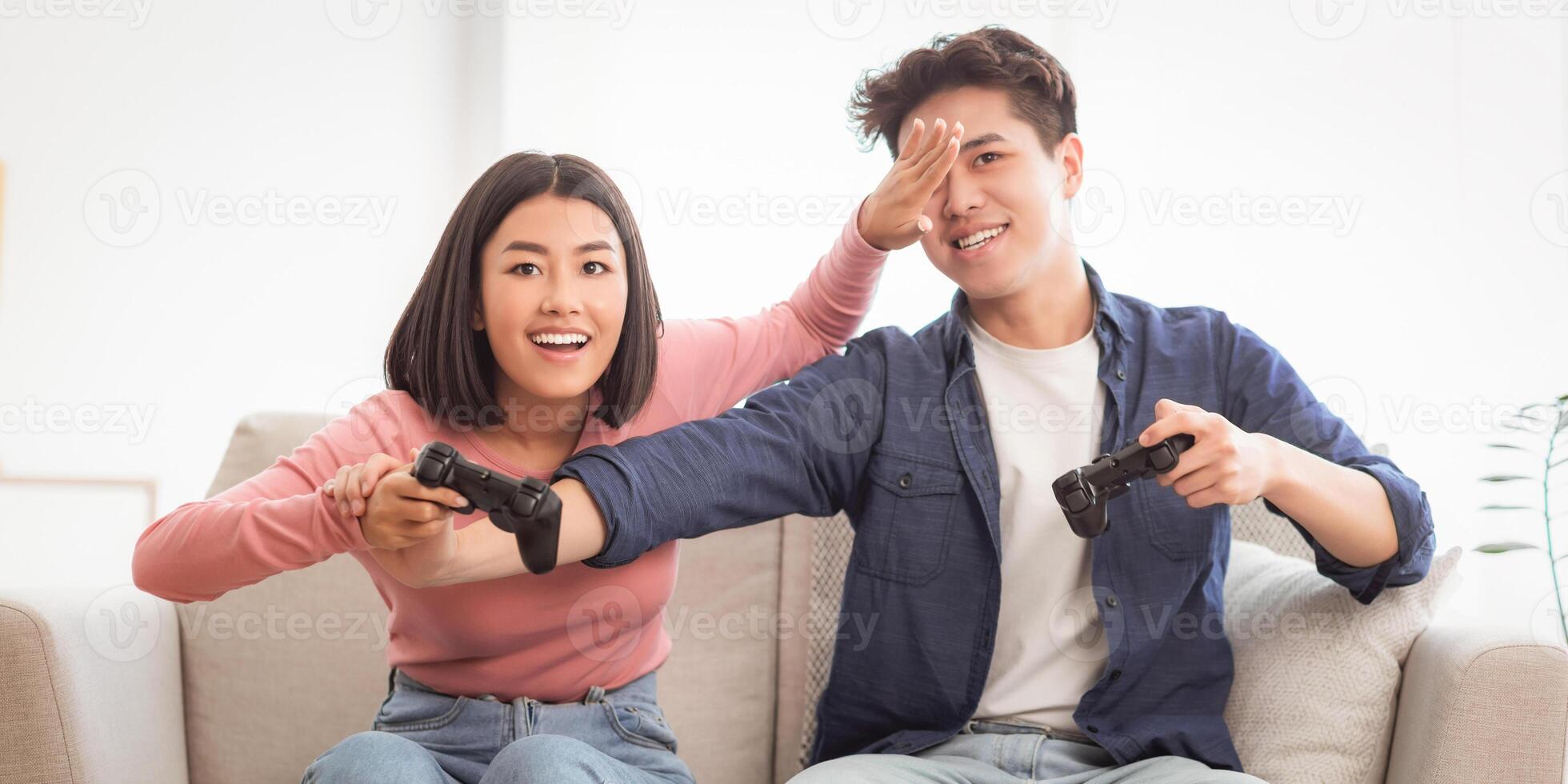 Cheerful Asian Spouses Having Fun Playing Game Together Sitting On Sofa Indoors. Chinese Girlfriend And Boyfriend Play Videogames At Home On Weekend. Computer Gaming Concept photo