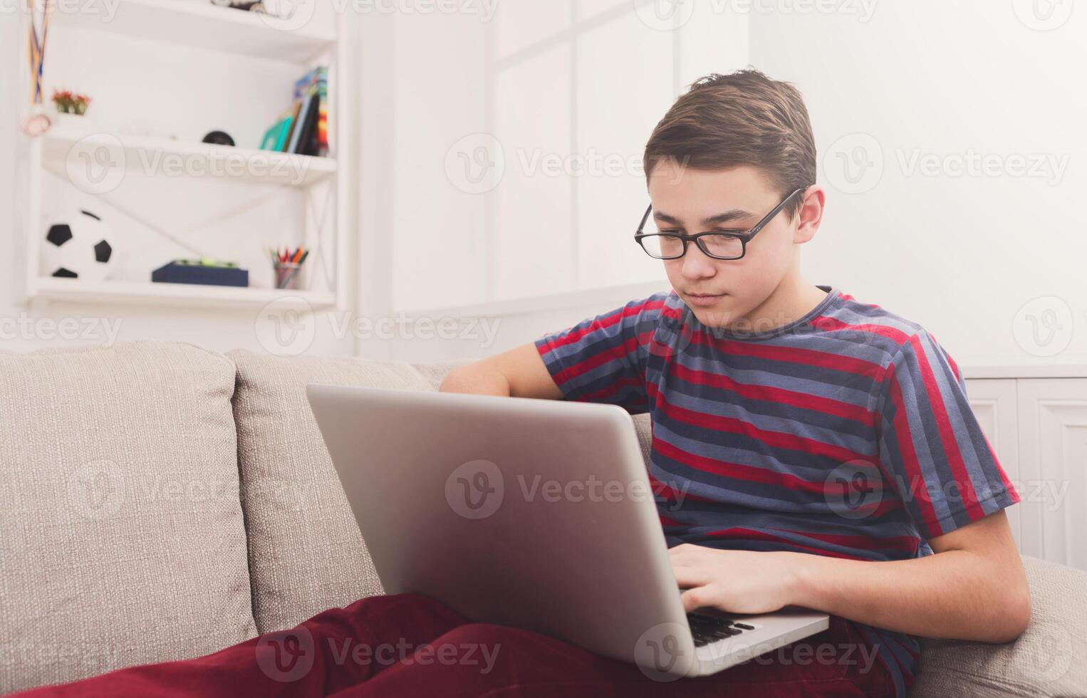 Teenager with computer on sofa at home. Boy engrossed in internet, typing on keyboard photo