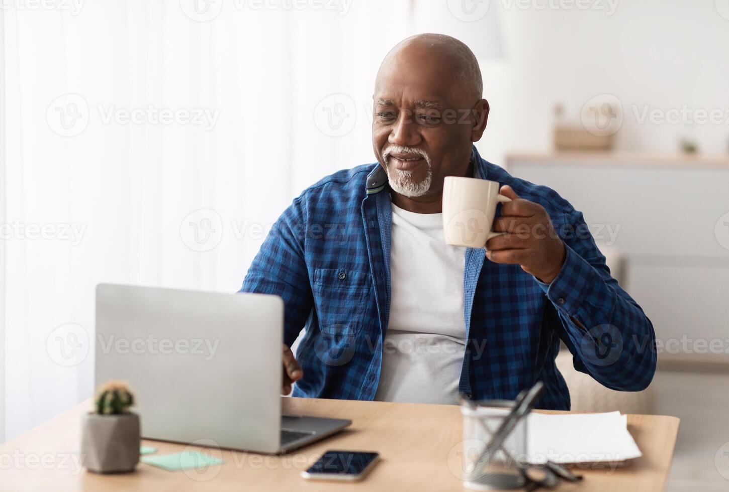 Black Mature Man Working Online On Laptop Computer And Drinking Coffee Sitting At Workplace In Modern Office. Entrepreneurship Career And Freelance Job In Senior Age Concept photo