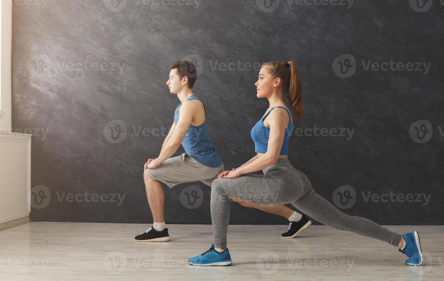 Fitness couple warmup stretching training at gray background indoors. Young man and woman making aerobics exercise at gym, copy space photo
