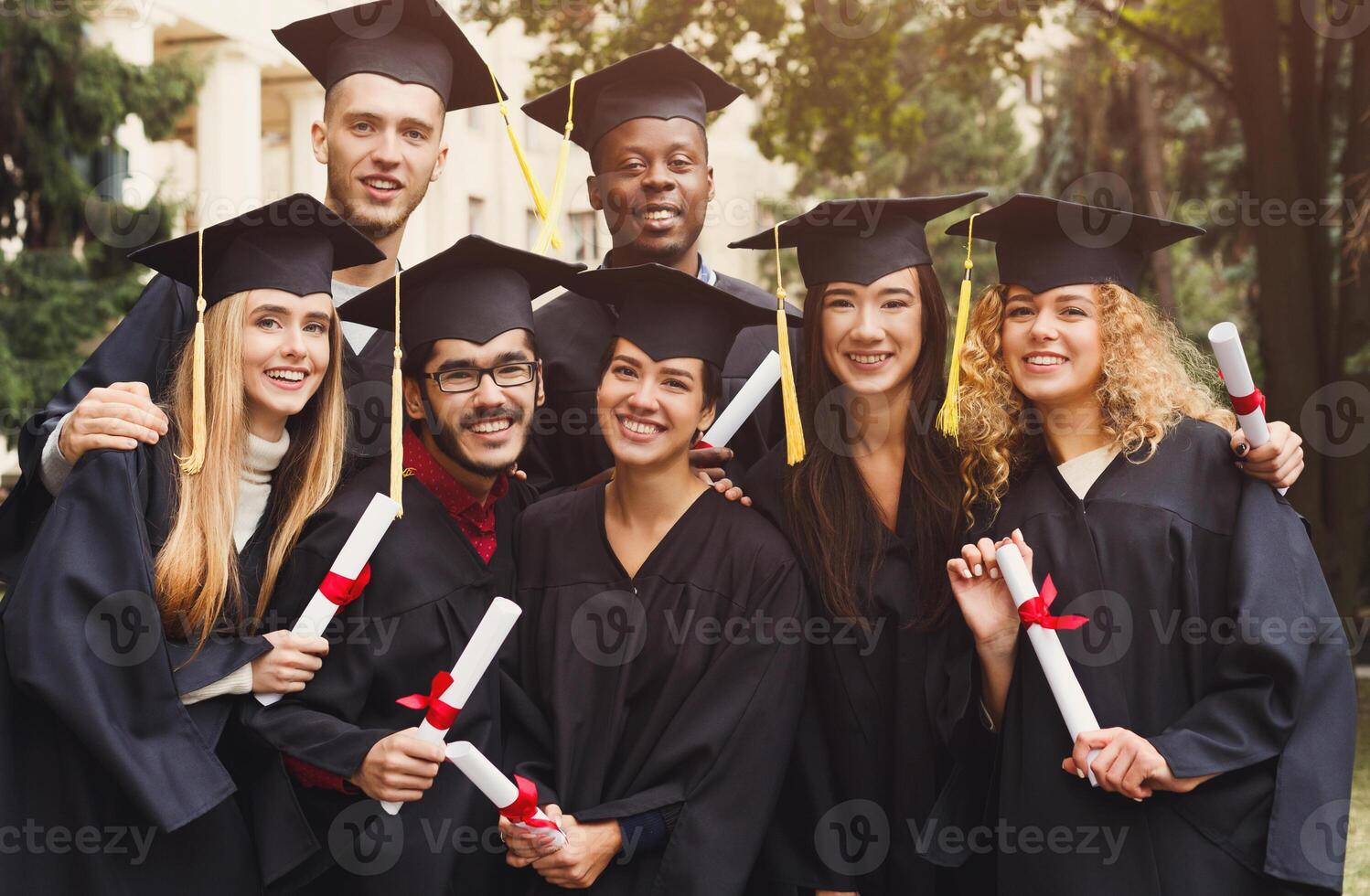Multiethnic students taking group photo to celebrate their graduation day, copy space. Education, qualification and gown concept.
