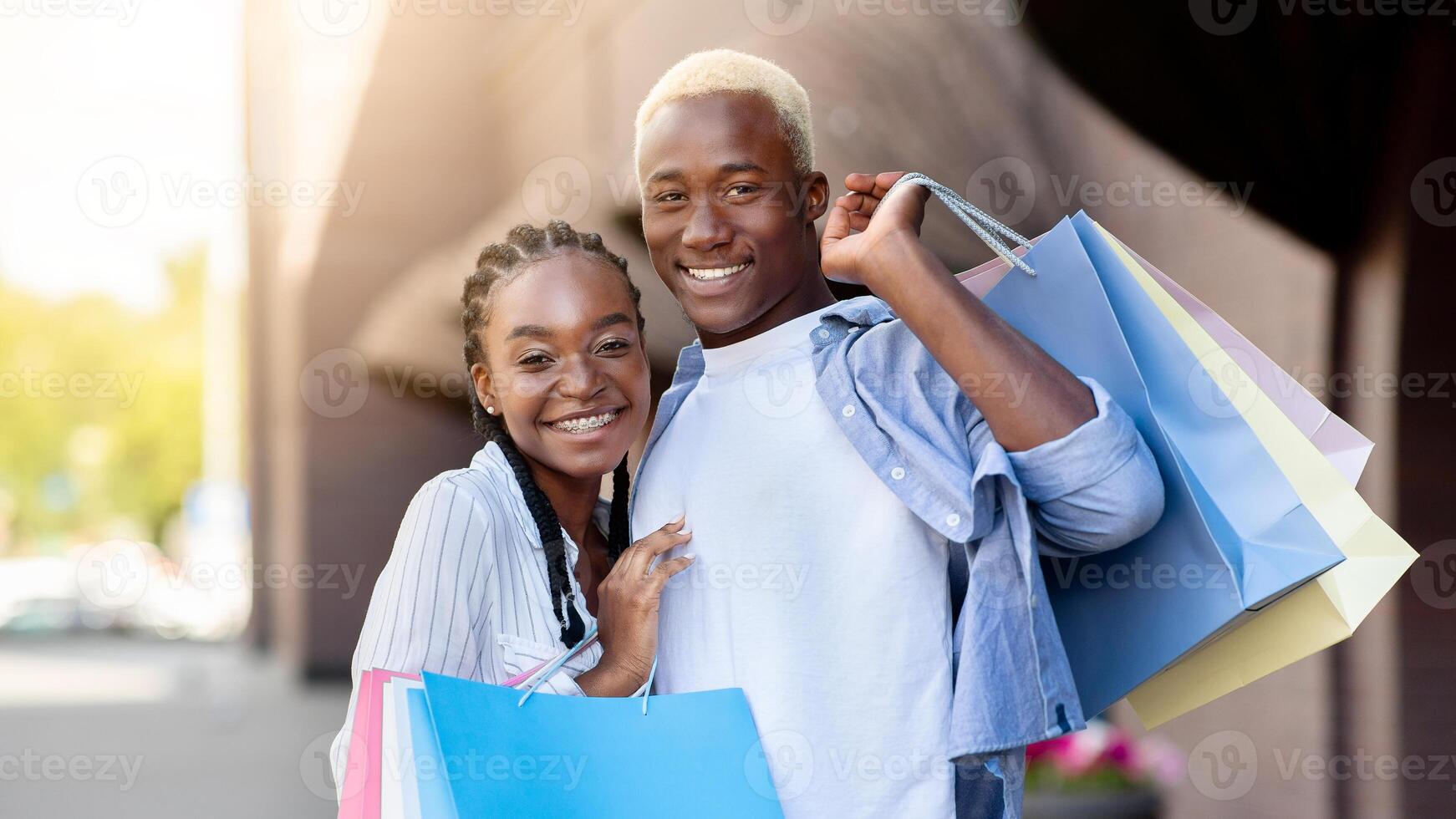 Closing of season and shopping. Smiling african american millennial man and woman with shopping bags hugs and looks at camera, near store, copy space photo