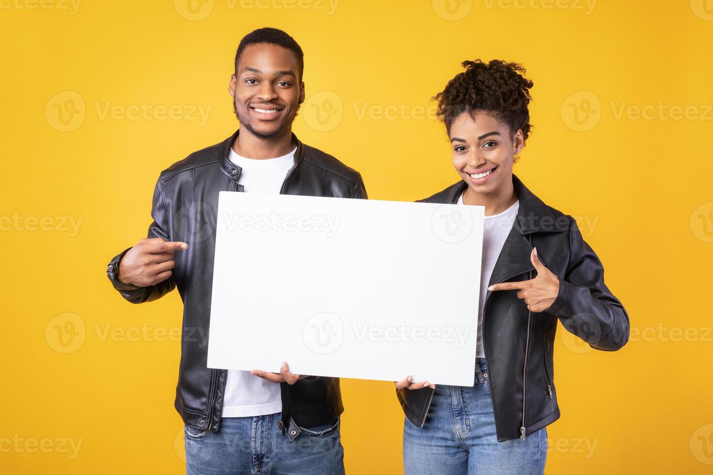 Positive Black Couple Showing Blank White Board Pointing Fingers At Free Space For Text Advertising Something Standing Over Yellow Studio Background. Advertisement Banner Concept photo
