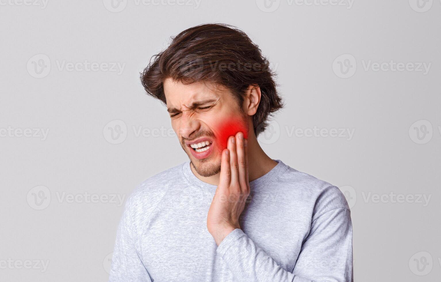 Endure pain. Sad man suffers from pain in his teeth and presses hand to red spot, isolated on gray background, studio shot, panorama photo