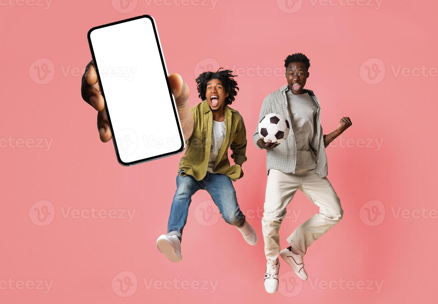 Overjoyed male friends jumping and showing big smartphone with empty white screen, excited black guys celebrating win, pink studio background, mock up collage banner photo