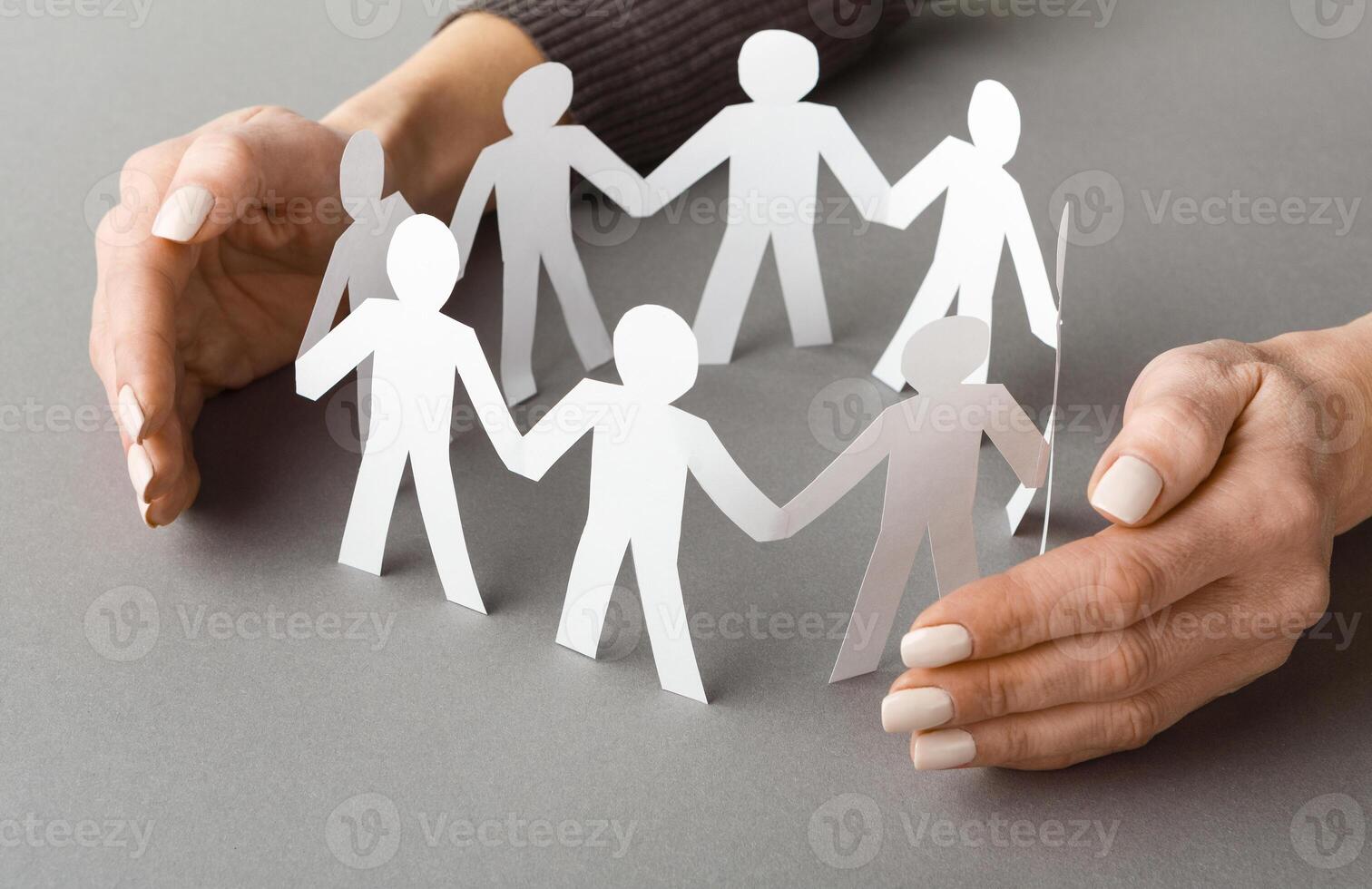 Leadership and care. Businessperson's hands protecting paper cut out figures on gray background, copy space photo