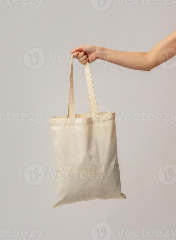 Closeup Shot Of Female Hand Carrying Blank Eco Canvas Tote Bag, Unrecognizable Woman Enjoying Sustainable Shopping With No Plastic Waste, Standing Over Light Grey Studio Background, Copy Space photo