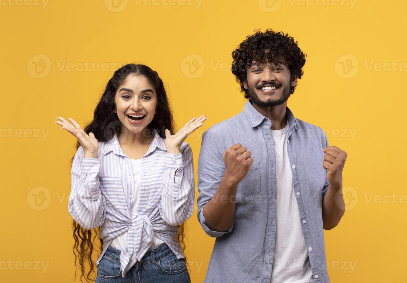 Wow. Overjoyed indian spouses gesturing in amazement looking at camera over yellow studio background. Emotional surprised couple gesturing yes photo
