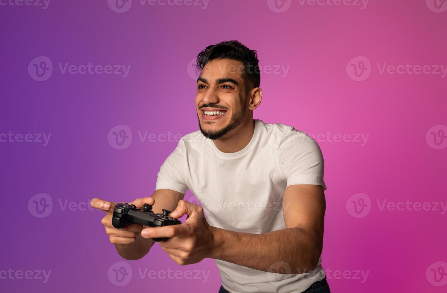Happy young Arab guy with joystick playing game in neon light. Millennial middle Eastern gamer with controller participating in online gaming championship. Modern hobbies concept photo