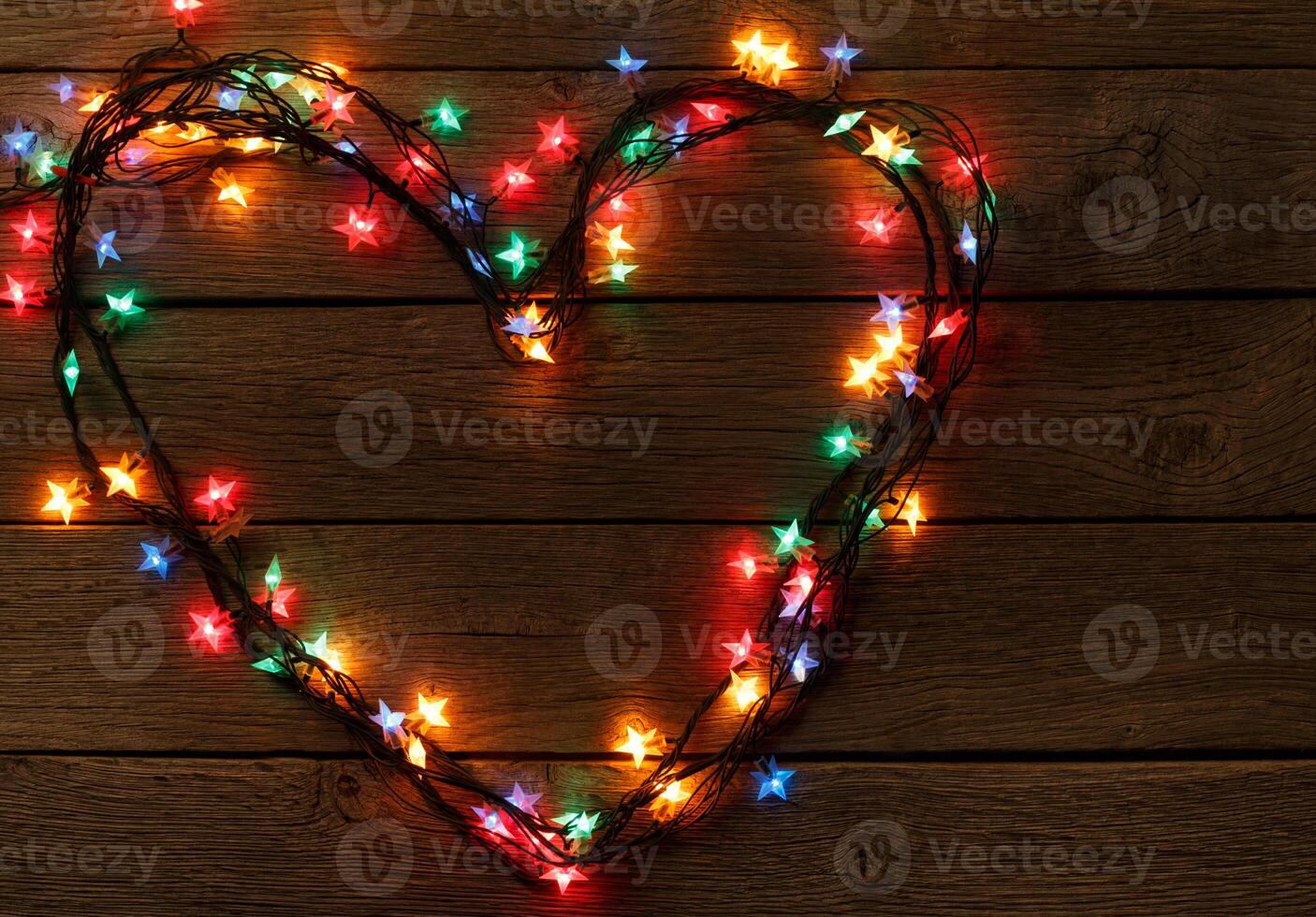 Christmas star lights background. Holiday shiny garland border in heart shape love symbol top view on brown wooden planks surface. Xmas tree decorations, winter holidays illumination photo