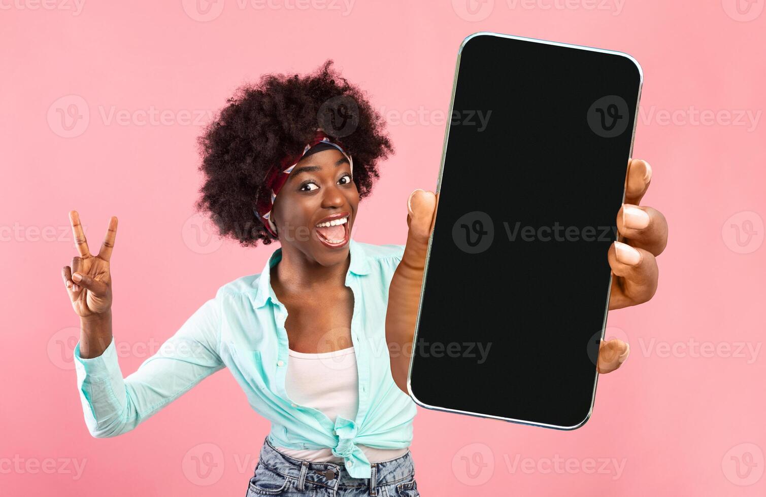 Great App. Cheerful Excited Black Woman Holding Smartphone With Blank Screen And Gesturing Peace, Funny African American Female Recommending New Mobile Application Or Website, Mockup Image photo