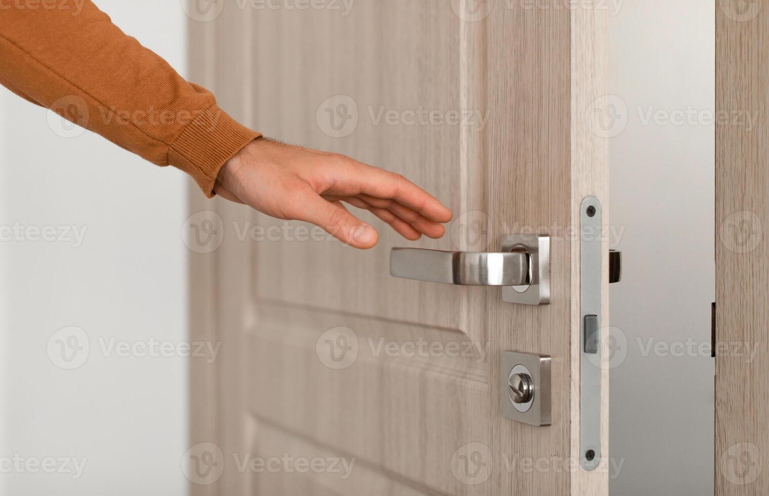 Closeup view of young unrecognizable man opening wooden door, reaching hand to handle doorknob, male visitor standing in entrance or exit, guest person wants to come in or leave, selective focus photo
