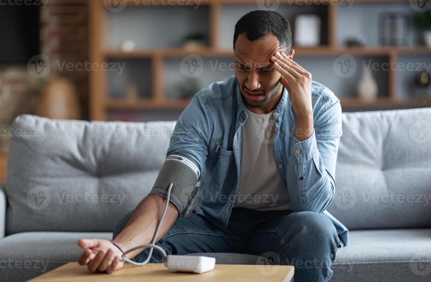 Sick Young Black Man Checking Blood Pressure With Modern Tonometer At Home, African American Guy Sitting On Couch And Using Electronic Sphygmomanometer, Ill Male Suffering Hypertension, Copy Space photo