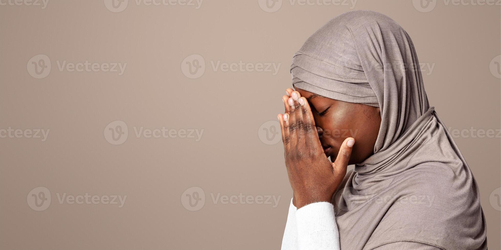 Upset black islamic lady in hijab covering face with hands, depressed african muslim woman in headscarf standing over light background, feeling ashamed, profile portrait with copy space photo
