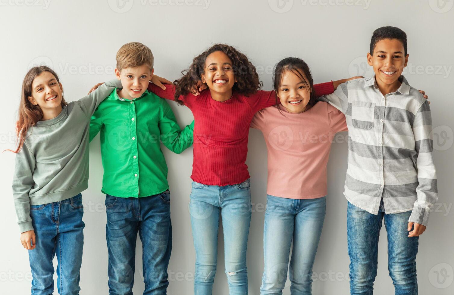 Cheerful Multiethnic Children Hugging Posing Smiling To Camera Indoors. Preteen Boys And Girls Standing Together Over Gray Wall. Childhood And Friendship Concept. photo