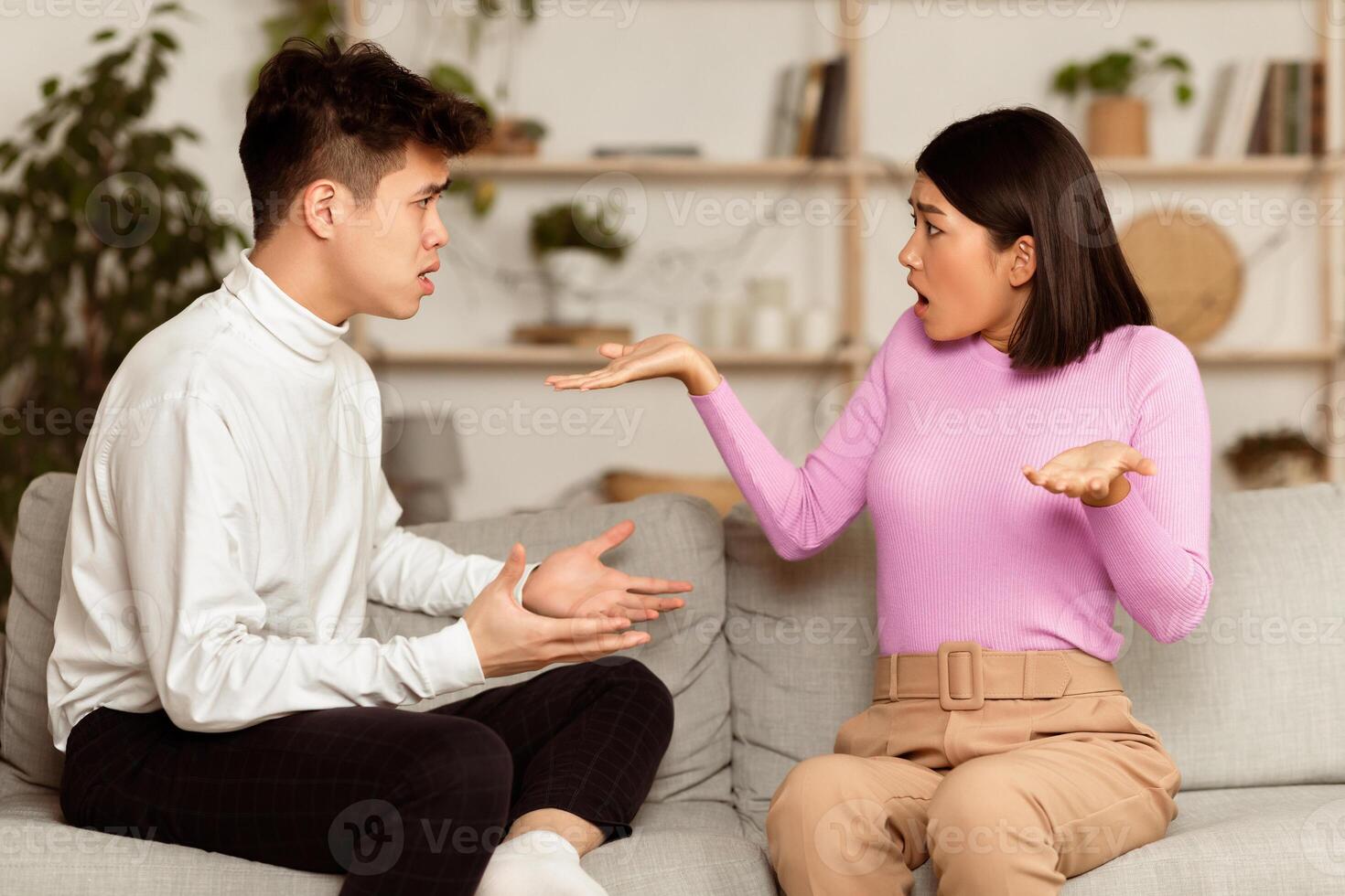 Asian Spouses Having Quarrel Sitting On Sofa At Home. Romantic Relationship Problems, Breakup And Divorce Concept. Chinese Family Couple Arguing Having Conflict. photo