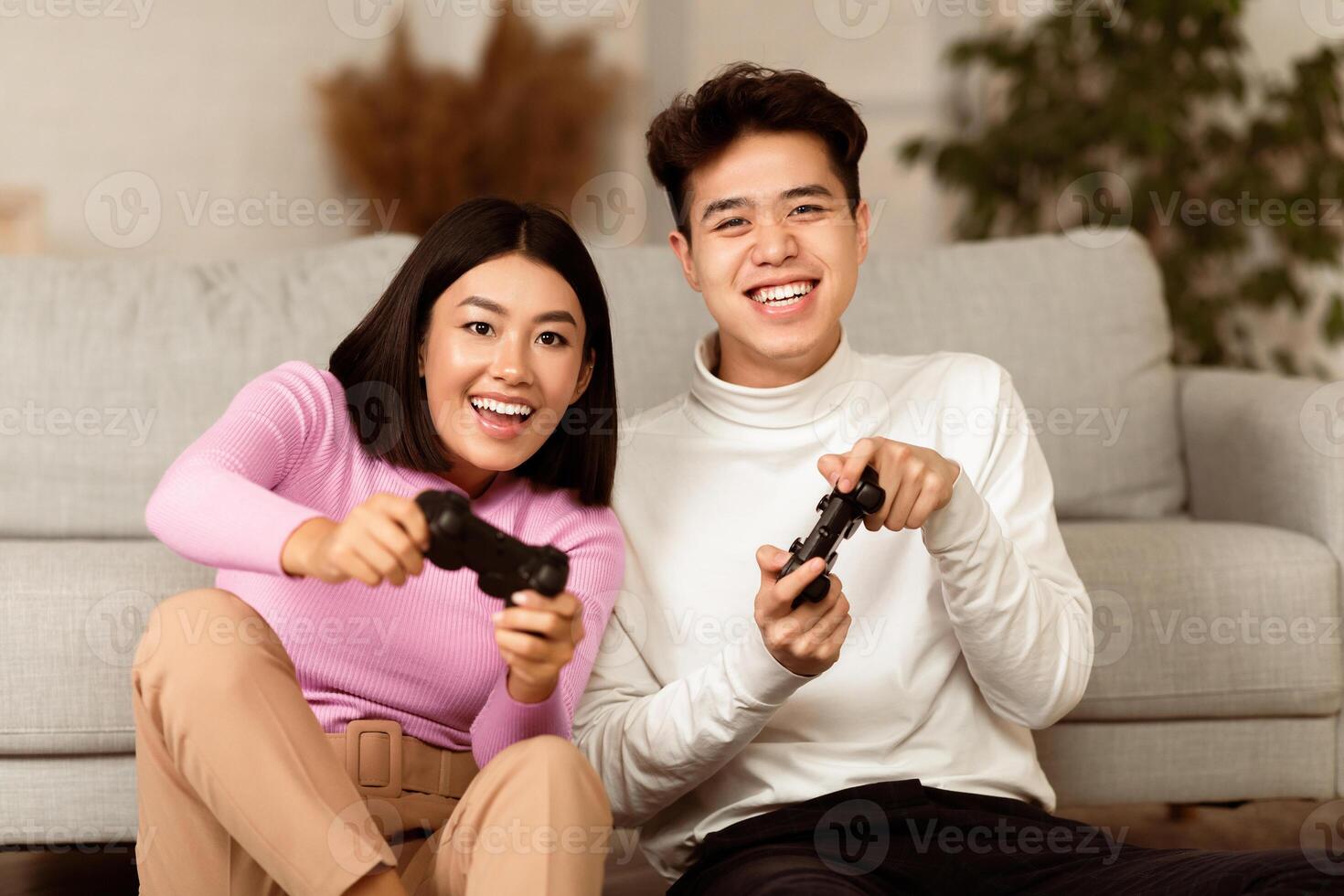Joyful Chinese Couple Playing Game Holding Joysticks Sitting On Sofa At Home On Weekend. Asian Boyfriend And Girlfriend Play Videogames. Family Fun, Computer Gaming And Games Concept photo