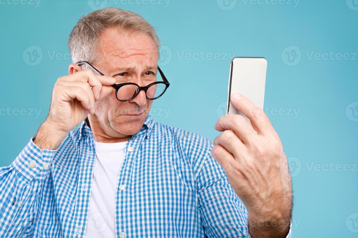 Poor Eyesight. Senior Man Squinting Eyes Reading Message On Phone Wearing Eyeglasses Having Problems With Vision, Blue Studio. Ophtalmic Issue, Bad Sight In Older Age, Macular Degeneration Concept photo