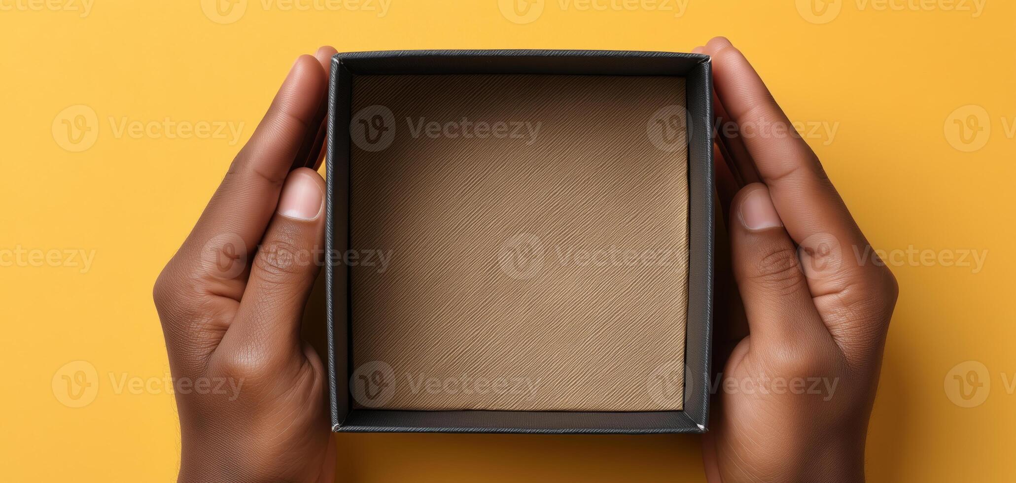 Two hands grip an open box revealing a plain interior. The box is centered against a vibrant yellow background, showcasing the anticipation of unpacking a delivery. photo