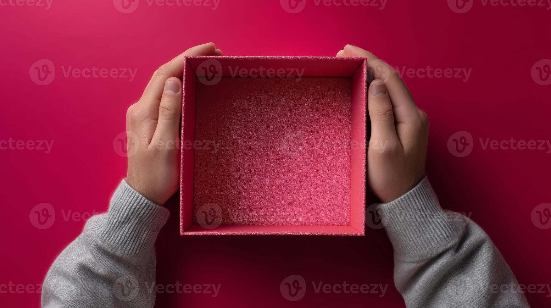 Hands grasp an empty, open box with a textured interior, placed on a bright pink surface. The moment captures the anticipation of receiving a delivery, highlighting the excitement of unboxing. photo