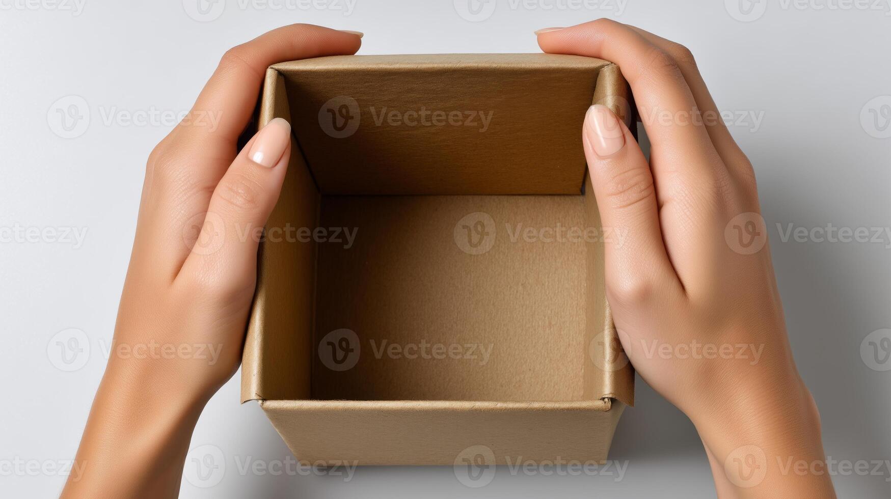 Two hands grasp an empty cardboard delivery box set on a smooth surface. The box is open, indicating the anticipation of unpacking new items. The setting is minimal and organized. photo