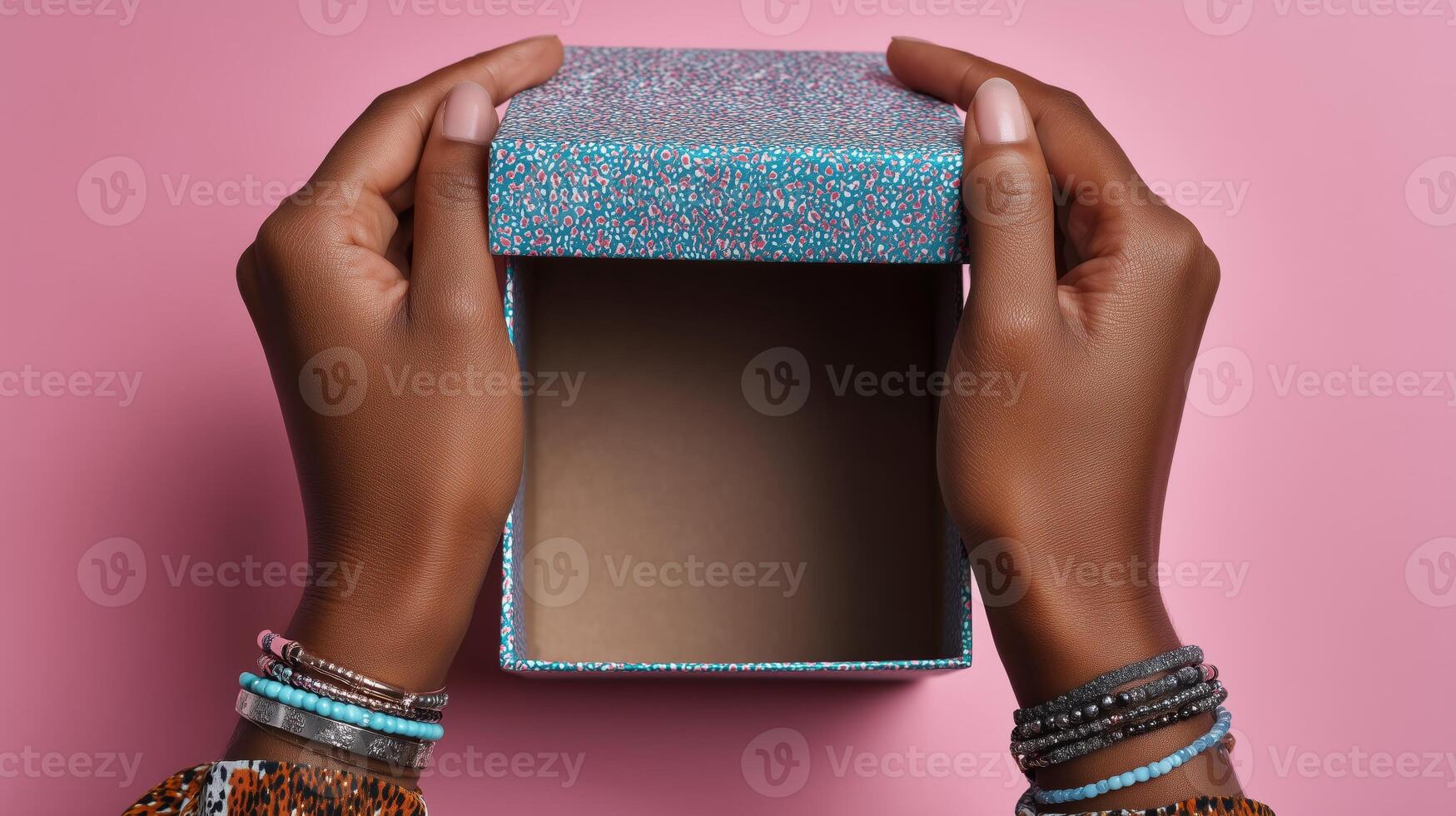 A pair of hands gently lifting the lid off a vibrant box featuring a textured surface. The box rests on a soft pink background, showcasing the anticipation of discovering its contents. photo