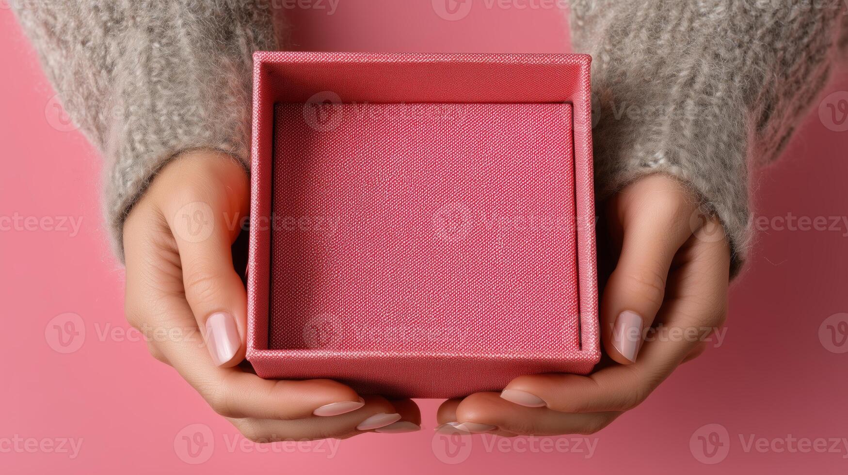 A pair of hands gently holds an open pink box against a soft pink background. The box appears empty and ready for a special delivery or a thoughtful gift. Warm, cozy textures highlight the scene. photo