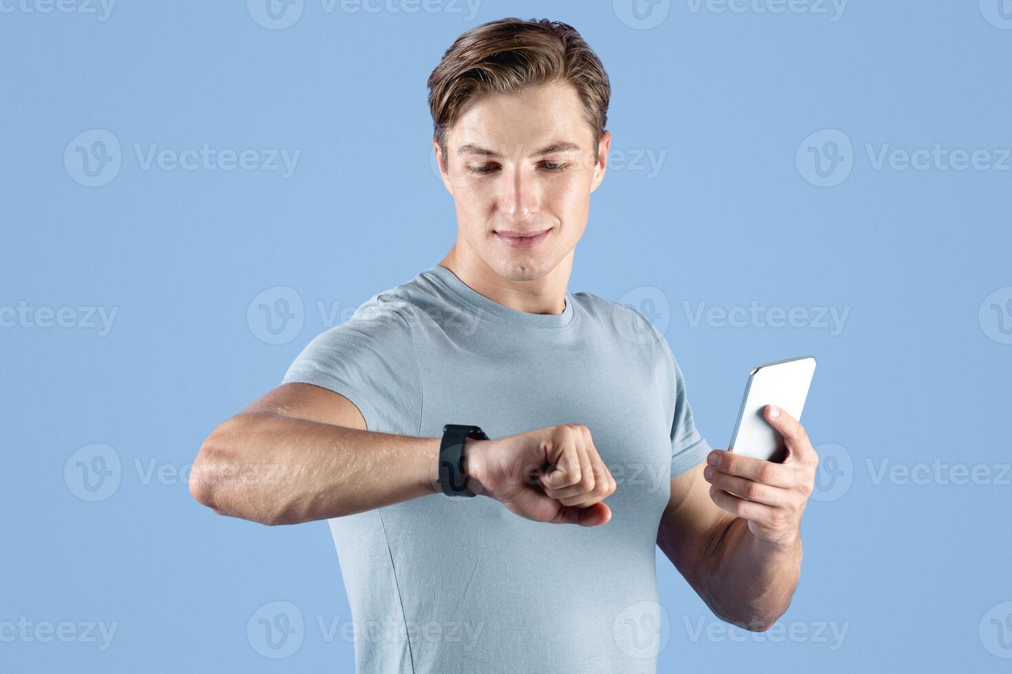 Active millennial guy with smartwatch and cellphone over violet studio background. Young athlete checking his fitness tracker data or body vitals during training. Sports and modern technologies photo