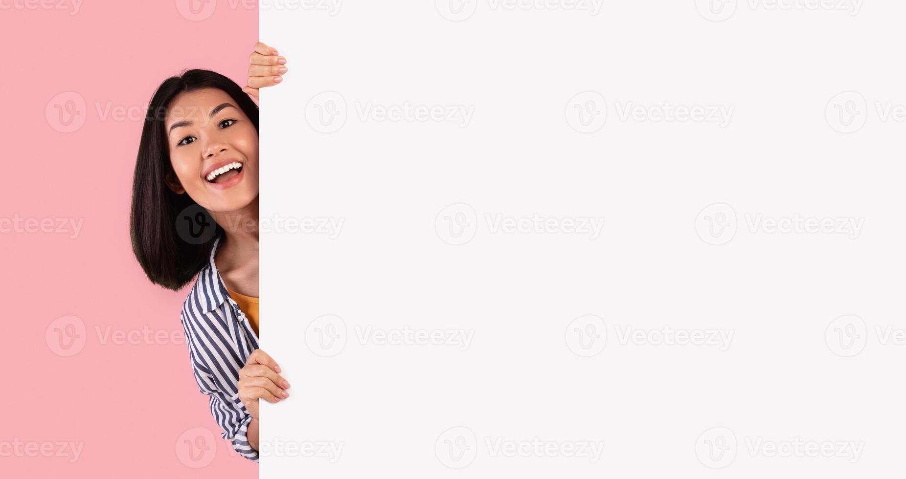 Intresting Offer. Happy Casual Asian Woman Peeping Out The Side Of White Advertisement Board For Your Text Or Design. Smiling Lady Holding Billboard, Looking At Camera, Standing Over Pink Wall photo