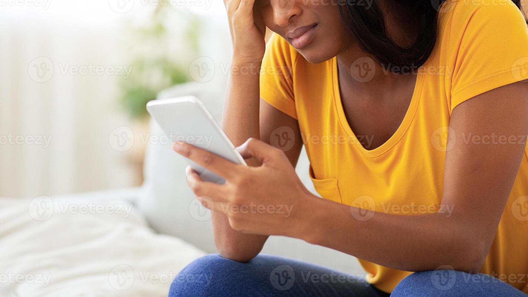 Unhappy African American lady looking at her smartphone with disgust indoors, copy space. Stressed black woman feeling depressed or suffering from headache after receiving terrible news on phone photo