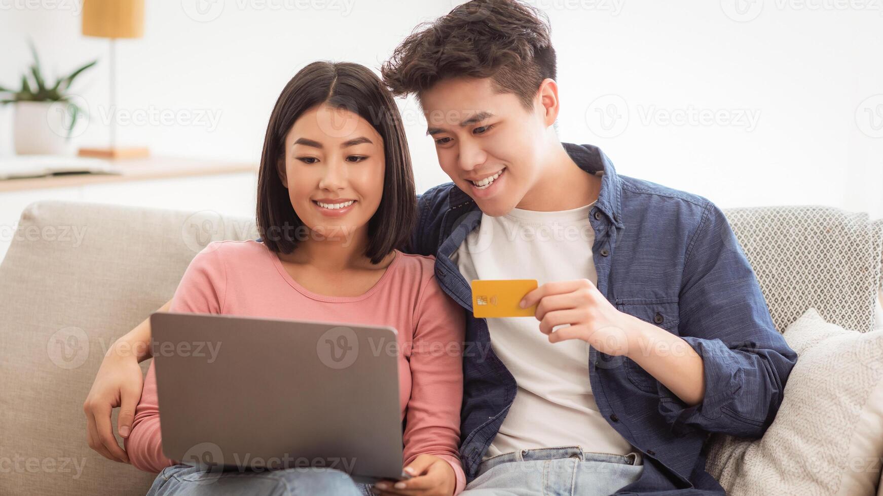 Chinese Family Couple Shopping Online With Laptop And Credit Card Paying For Order In Internet Store Sitting On Couch At Home. Happy Customers Buying And Purchasing Things On Weekend Concept photo