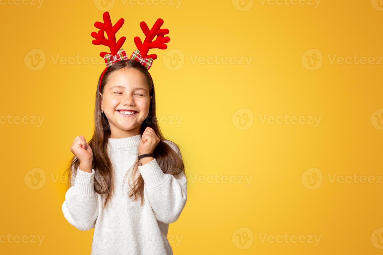 Feels euphoric. Happy little girl in sweater, with horns, closed eyes, isolated on yellow background, studio shoot photo