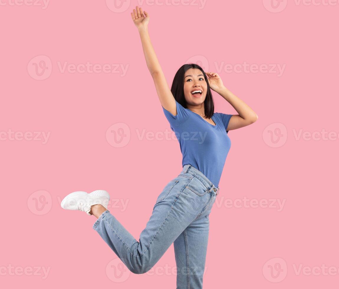 Time To Relax. Portrait of happy young asian woman jumping, dancing and raising hand up high, carefree lady being in a good mood, isolated over bright pink background, studio shot photo