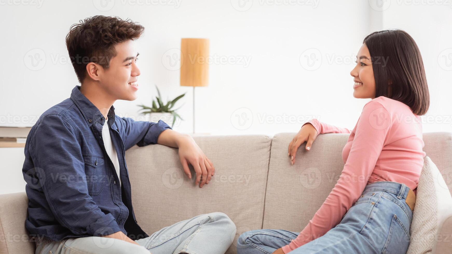 Dating And Flirt. Lovely Asian Couple Talking Enjoying Conversation Sitting On Sofa In Living Room At Home. Romantic Weekend And Communication In Relationship Concept photo