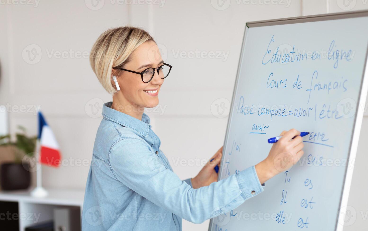 Friendly female teacher writing grammar rules on blackboard during online French lesson. Positive young tutor teaching foreign language on web. Remote education and tutoring concept photo